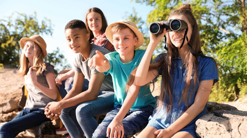 Eine Gruppe von Teens sitzt bei Sonnenschein auf Felsen und schaut erfreut in die Ferne